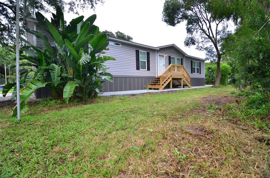 A single-story manufactured home with grey siding, a wooden staircase, and large tropical plants — 515 TWIN LAKES CIRCLE, LAKELAND, FL