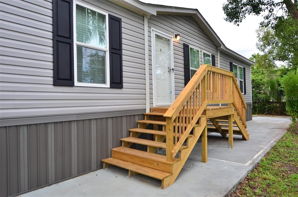 A gray manufactured home exterior features a wooden staircase leading to the front entrance — 515 TWIN LAKES CIRCLE, LAKELAND, FL