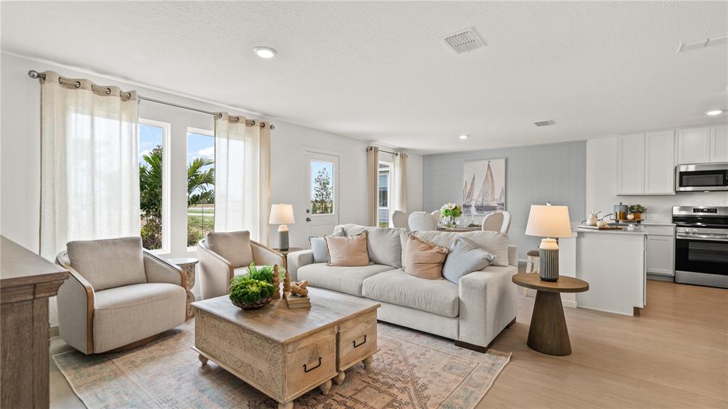An open-concept living room features a neutral sofa, two armchairs, a coffee table, and kitchen — 2243 AVEENO DRIVE, HAINES CITY, FL
