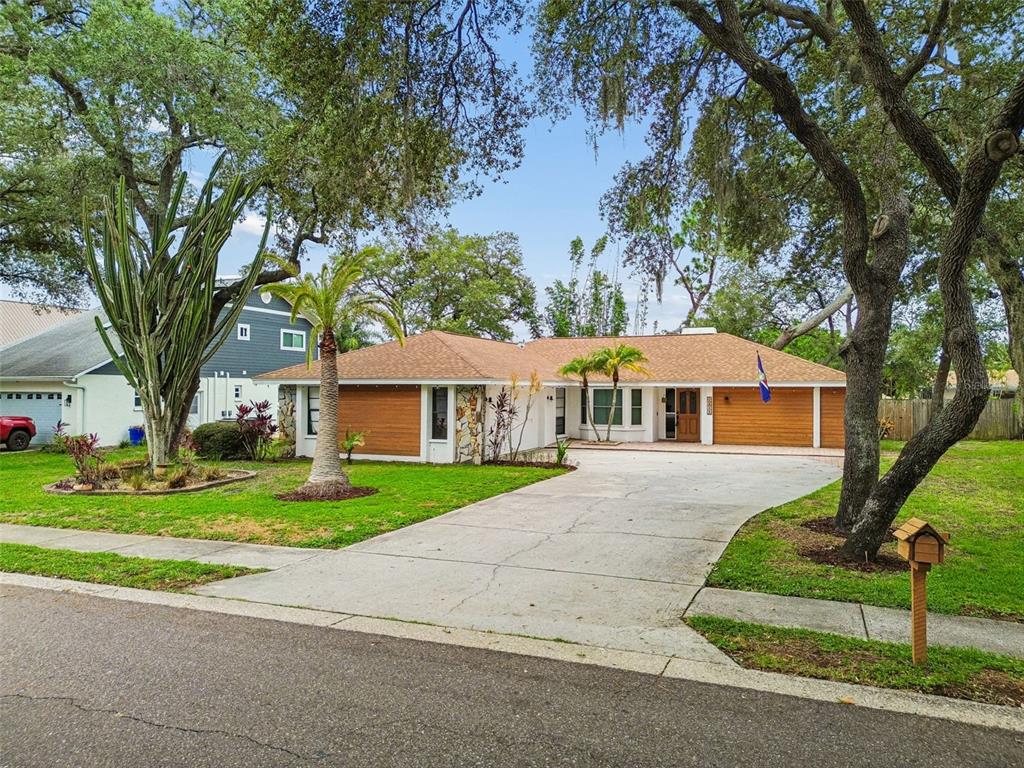 A single-story house with a concrete driveway, wood-paneled garage doors, and mature trees — 1425 POINSETTIA AVENUE, TARPON SPRINGS, FL