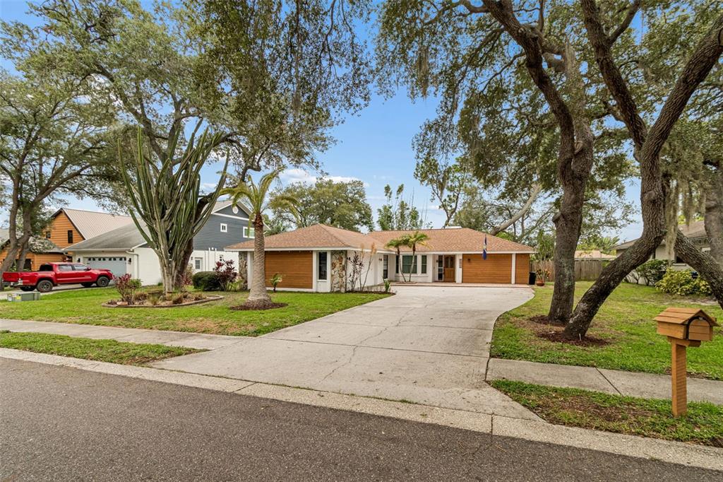 A single-story house with a concrete driveway, wood-paneled accents, and mature trees in the yard — 1425 POINSETTIA AVENUE, TARPON SPRINGS, FL