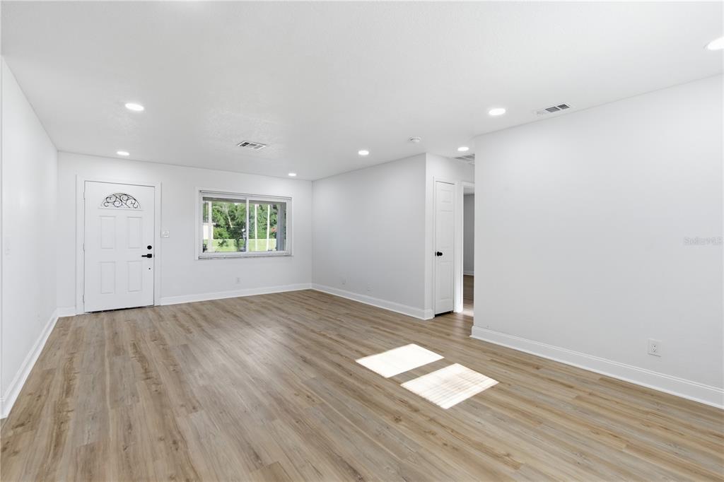 A bright, empty living room features light wood-look flooring, white walls, and a front door — 12760 118TH STREET, LARGO, FL