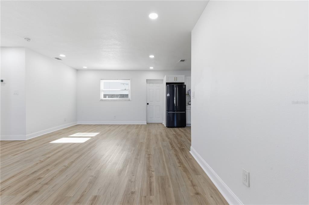 A bright, open-concept room features light wood-look flooring, white walls, recessed lighting, and a refrigerator — 12760 118TH STREET, LARGO, FL