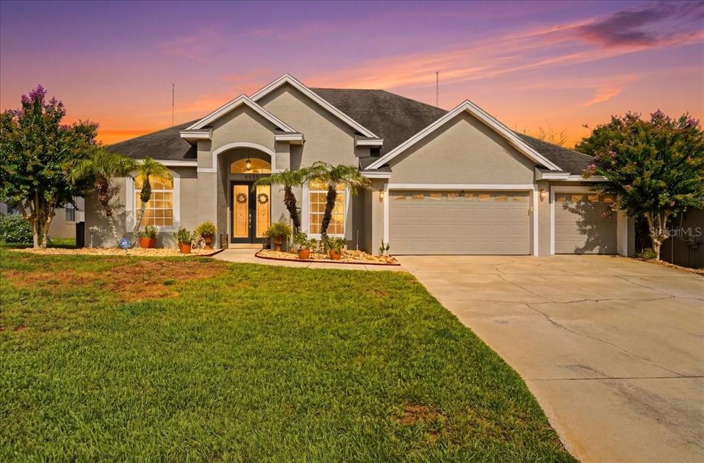 A single-story suburban house with a gray stucco exterior, a three-car garage, and landscaped yard — 6767 HILLIS DRIVE, LAKELAND, FL