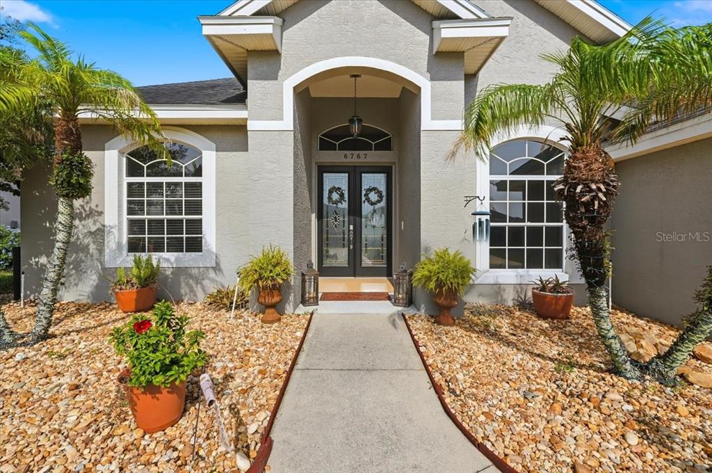The front exterior of a house features a concrete walkway, double doors, and palm trees — 6767 HILLIS DRIVE, LAKELAND, FL