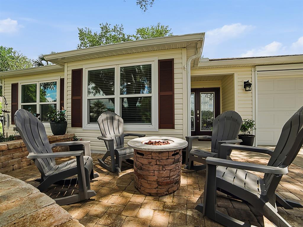 A patio features four gray rocking chairs arranged around a circular stone fire pit — 1033 ALOHA WAY, LADY LAKE, FL