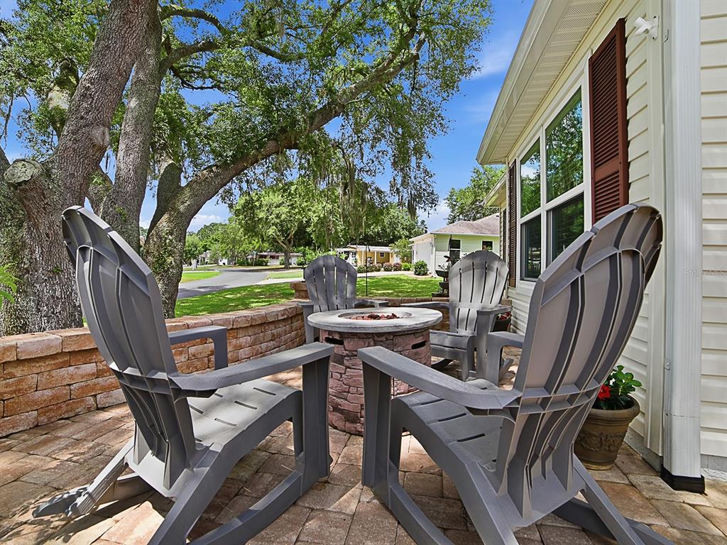 Four gray Adirondack chairs surround a stone fire pit on a brick patio — 1033 ALOHA WAY, LADY LAKE, FL