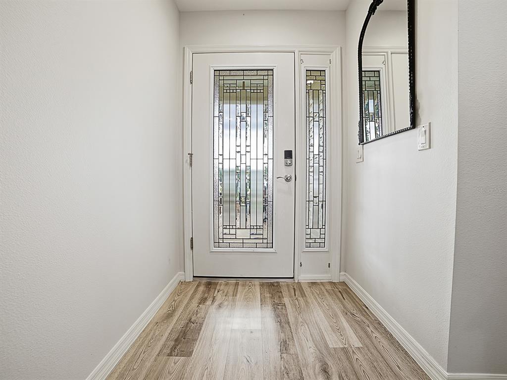A white front door with decorative glass panels opens into a foyer with wood-look flooring — 1033 ALOHA WAY, LADY LAKE, FL