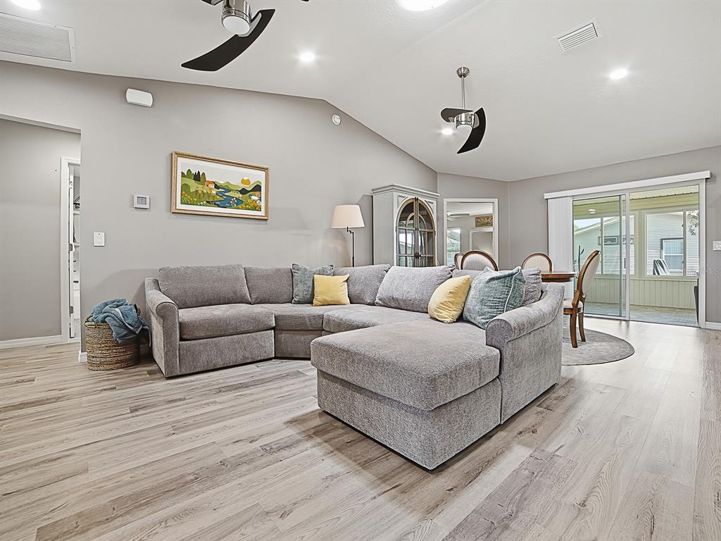 A living room features a gray sectional sofa, wood-look flooring, and a vaulted ceiling — 1033 ALOHA WAY, LADY LAKE, FL