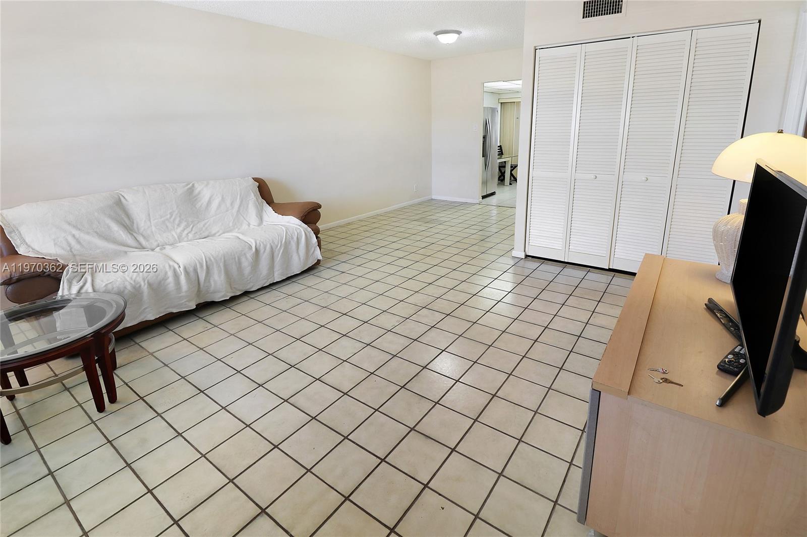 A living room features white tiled floors, a brown sofa with a cover, and louvered closet doors — 601 NW 78th Ter # 204, Margate FL 33063, MARGATE, FL