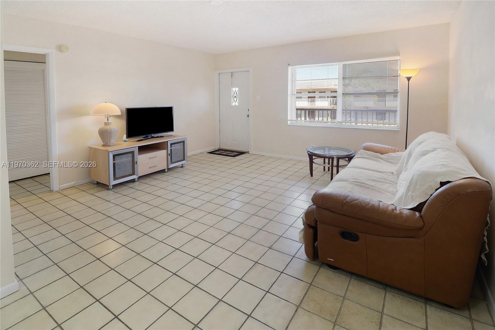 A living room features light-colored tile flooring, a brown leather sofa, and a television console — 601 NW 78th Ter # 204, Margate FL 33063, MARGATE, FL
