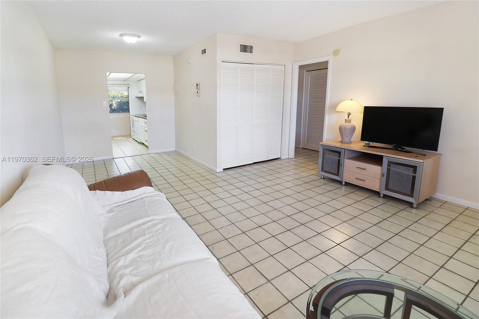 A living room features white walls, tiled floors, a television console, and an adjacent kitchen — 601 NW 78th Ter # 204, Margate FL 33063, MARGATE, FL