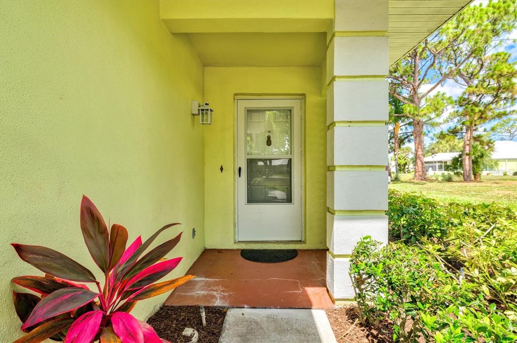 A light yellow exterior wall features a white storm door and a decorative plant — 316 WEXFORD TERRACE UNIT 167, VENICE, FL