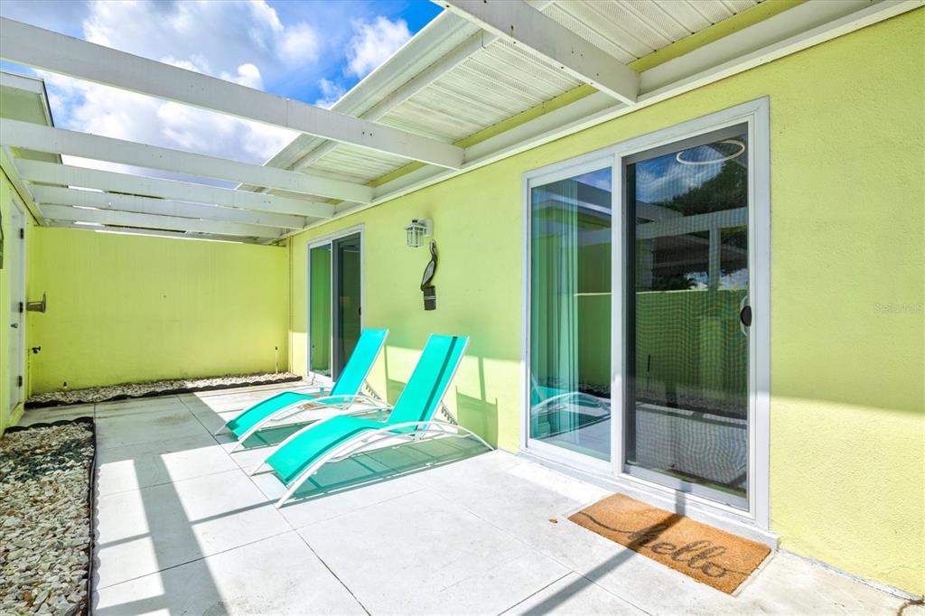 A patio with two turquoise lounge chairs, a sliding glass door, and a white pergola — 316 WEXFORD TERRACE UNIT 167, VENICE, FL