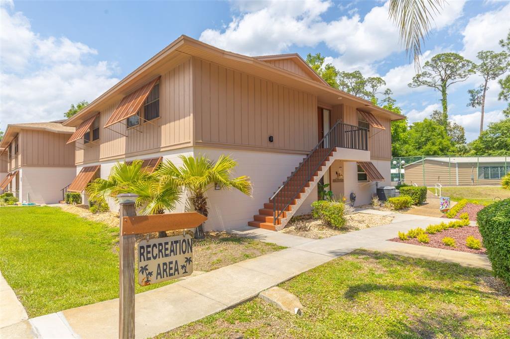 A two-story apartment building with exterior stairs and a recreation area sign in the foreground — 180 MAGNOLIA WOODS COURT UNIT 15B, DELTONA, FL