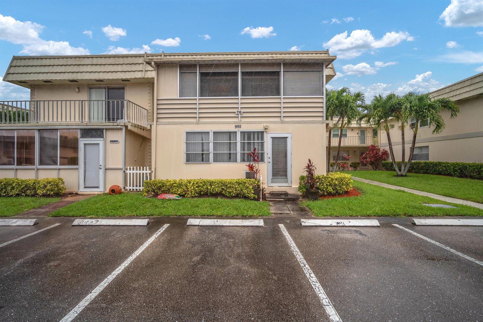 A two-story apartment building exterior features tan siding, a parking lot, and palm trees — 716 Saxony Place # O, Delray Beach FL 33446, DELRAY BEACH, FL