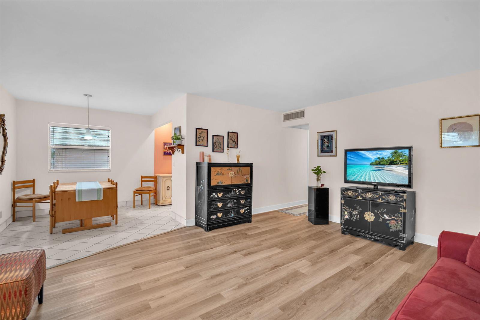 A living room with wood-look flooring, a black cabinet, and an adjacent tiled dining area — 716 Saxony Place # O, Delray Beach FL 33446, DELRAY BEACH, FL