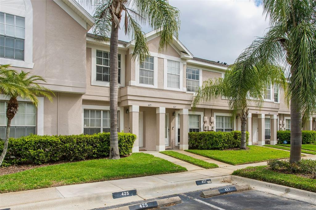 A two-story townhouse exterior with beige siding, palm trees, and designated parking spaces — 425 KENSINGTON LAKE CIRCLE, BRANDON, FL