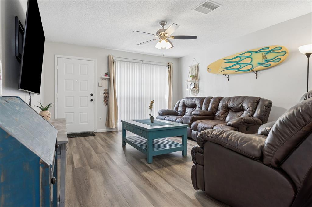 A living room features wood-look flooring, a brown leather sofa, a blue coffee table, and a surfboard — 425 KENSINGTON LAKE CIRCLE, BRANDON, FL