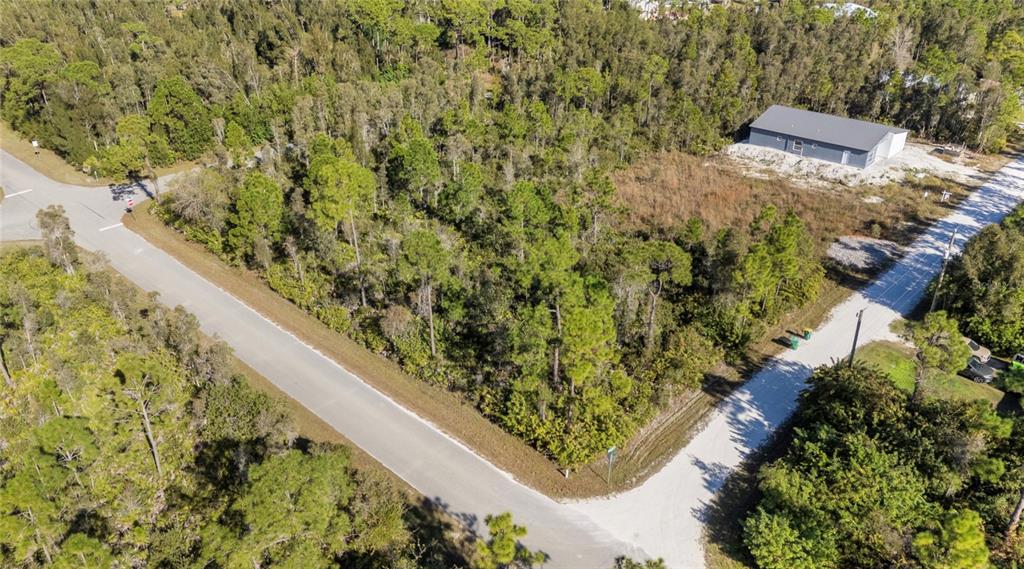 An aerial view shows a vacant, wooded corner lot bordered by paved and gravel roads — 12147 PLATANO DRIVE, PUNTA GORDA, FL