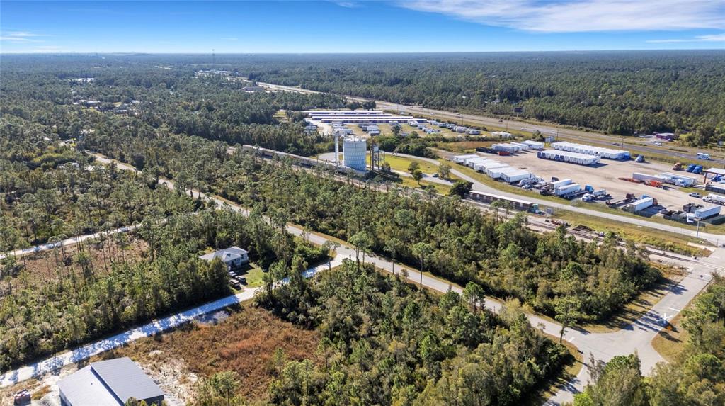 An aerial view shows a wooded lot, a nearby house, and a commercial storage facility — 12147 PLATANO DRIVE, PUNTA GORDA, FL