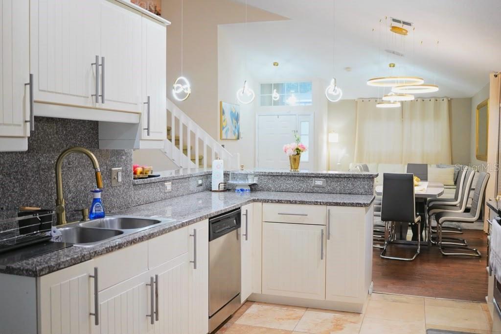 A kitchen with white cabinets and granite countertops overlooks a dining area and entryway — 2592 CHATHAM CIRCLE, KISSIMMEE, FL