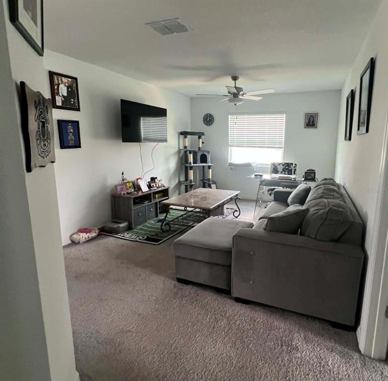 A living room features gray carpet, a sectional sofa, a television, and a coffee table — 8845 GALLANTREE PLACE, LAND O LAKES, FL