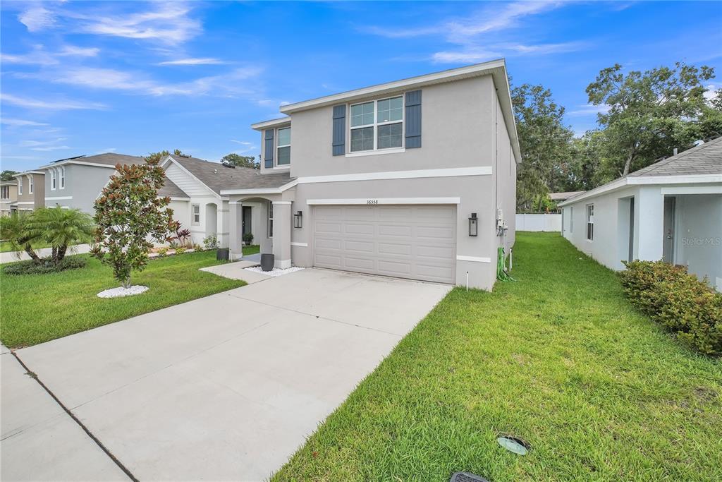 A two-story house with a beige stucco exterior, a two-car garage, and a concrete driveway — 36558 SPANISH ROSE DRIVE, DADE CITY, FL