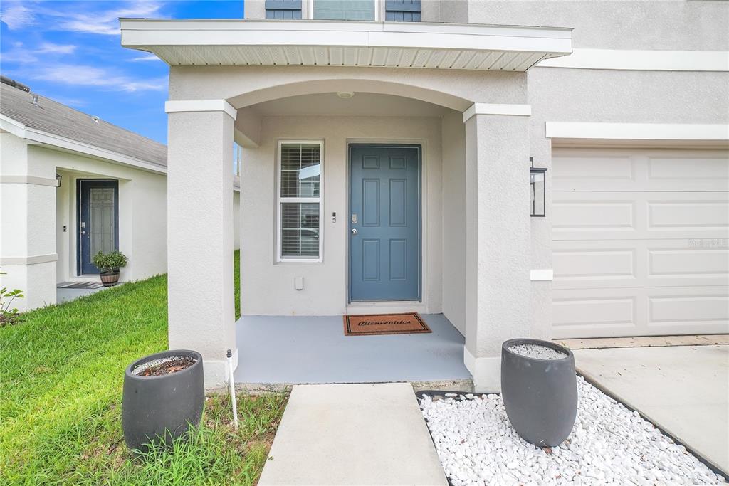 A front porch with a blue door, concrete walkway, and two large dark planters — 36558 SPANISH ROSE DRIVE, DADE CITY, FL