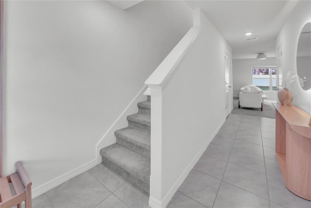 A carpeted staircase with a white railing sits next to a tiled hallway leading to a living area — 36558 SPANISH ROSE DRIVE, DADE CITY, FL
