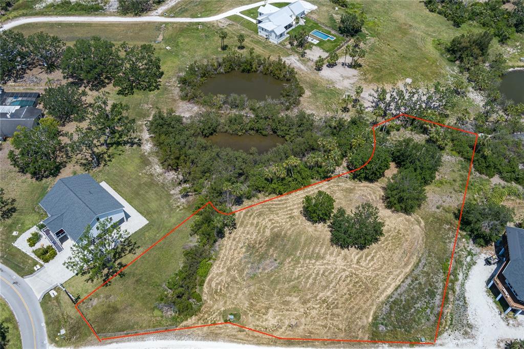 An aerial view shows a vacant, grass-covered lot outlined in red next to residential houses — 818 BAYOU POINT COURT, TERRA CEIA, FL