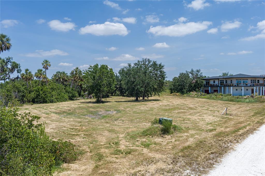 A grassy, vacant lot features scattered trees and a nearby multi-story building under a sky — 818 BAYOU POINT COURT, TERRA CEIA, FL
