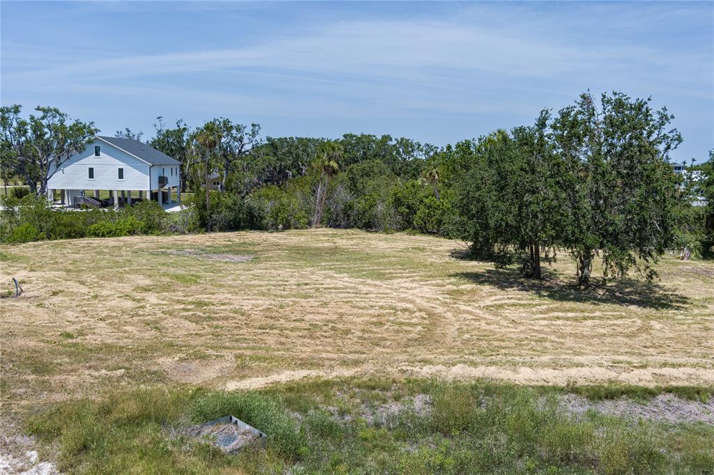A large, cleared grassy lot is surrounded by trees with a white house nearby — 818 BAYOU POINT COURT, TERRA CEIA, FL