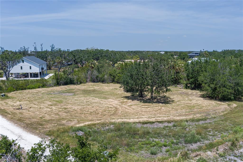 An elevated view of a cleared, grassy vacant lot surrounded by trees and nearby houses — 818 BAYOU POINT COURT, TERRA CEIA, FL