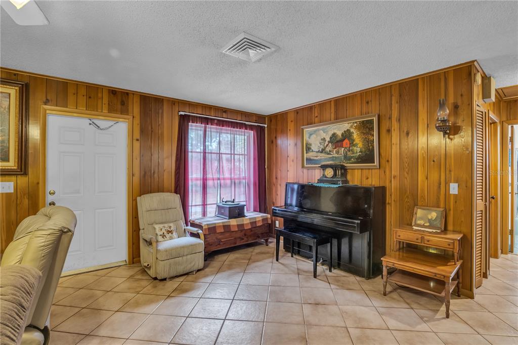 A room with wood-paneled walls, tile flooring, a piano, and a window with red curtains — 14181 35TH PLACE N, LOXAHATCHEE, FL