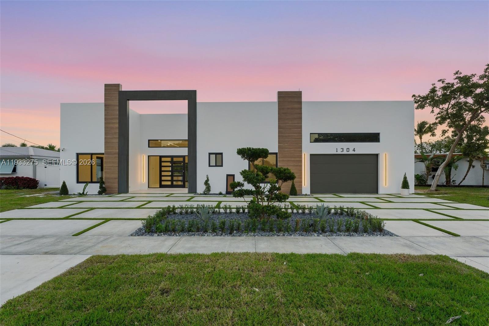 A modern, single-story house with a white facade, wood accents, and a paved driveway — 1304 SE 10th Ter, Deerfield Beach FL 33441, DEERFIELD BEACH, FL