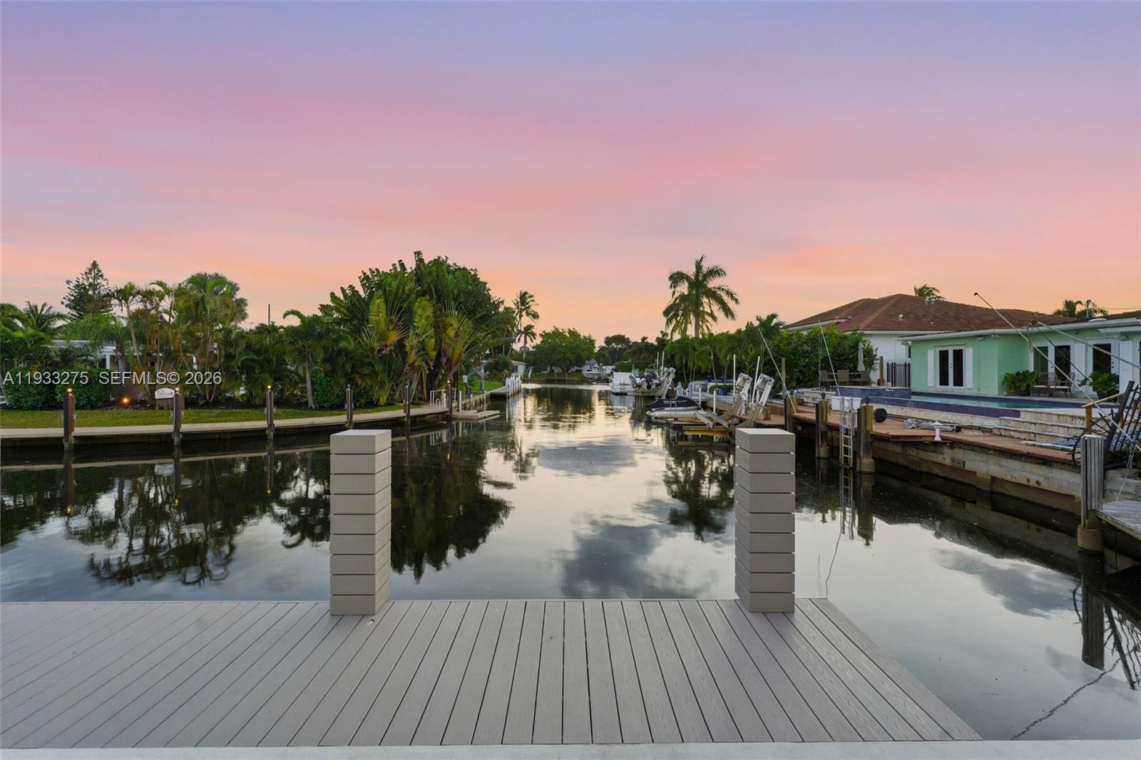 A wooden dock overlooks a canal lined with palm trees and residential properties at sunset — 1304 SE 10th Ter, Deerfield Beach FL 33441, DEERFIELD BEACH, FL
