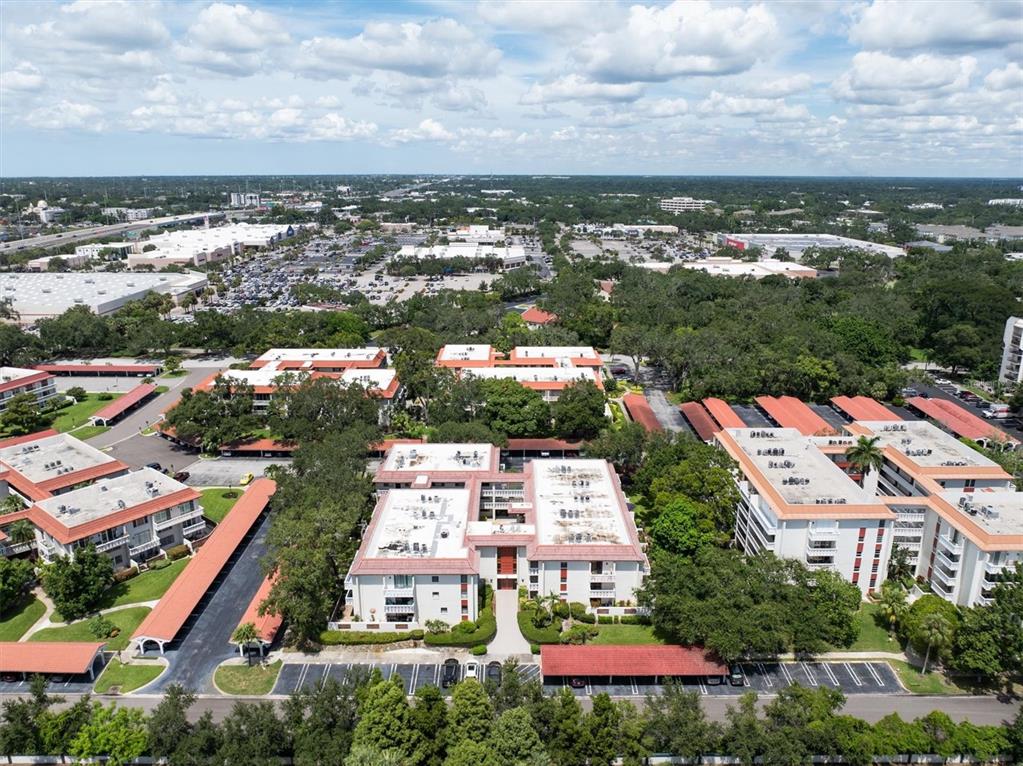 An aerial view shows several multi-story apartment buildings with red roofs and covered parking areas — 2612 PEARCE DRIVE UNIT 310, CLEARWATER, FL