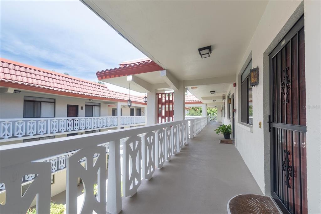 An outdoor walkway with white railings overlooks a courtyard in a multi-story apartment complex — 2612 PEARCE DRIVE UNIT 310, CLEARWATER, FL