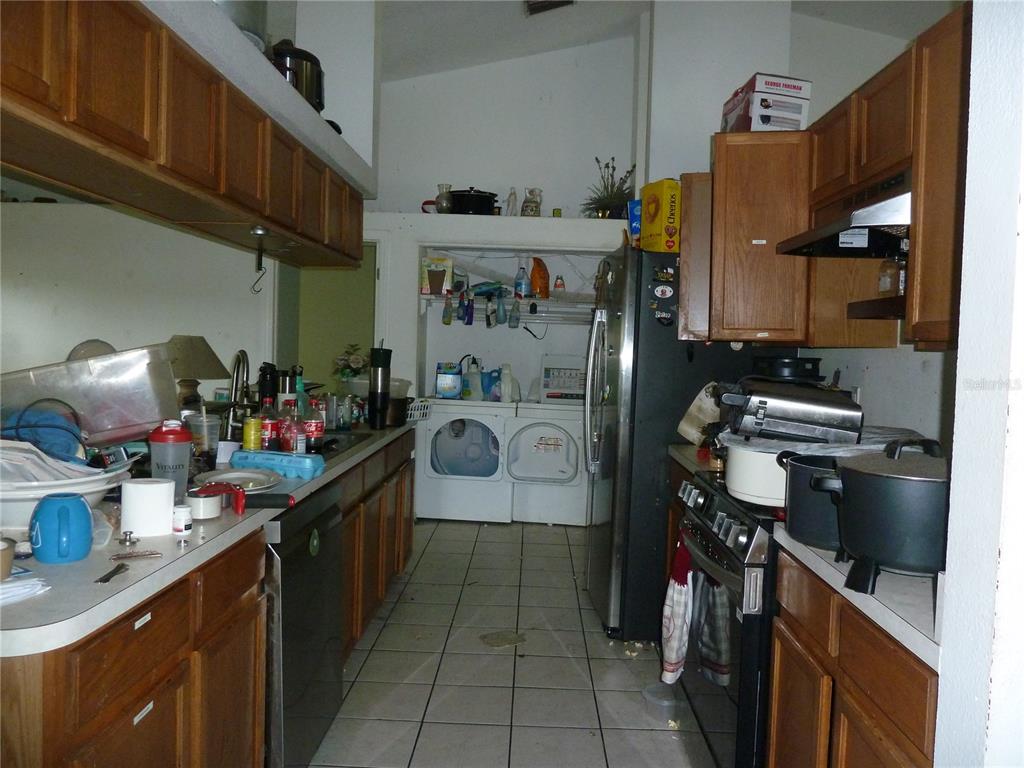 A kitchen with wooden cabinets, tile flooring, and a laundry area at the far end — 5 S JUPITER AVENUE, CLEARWATER, FL