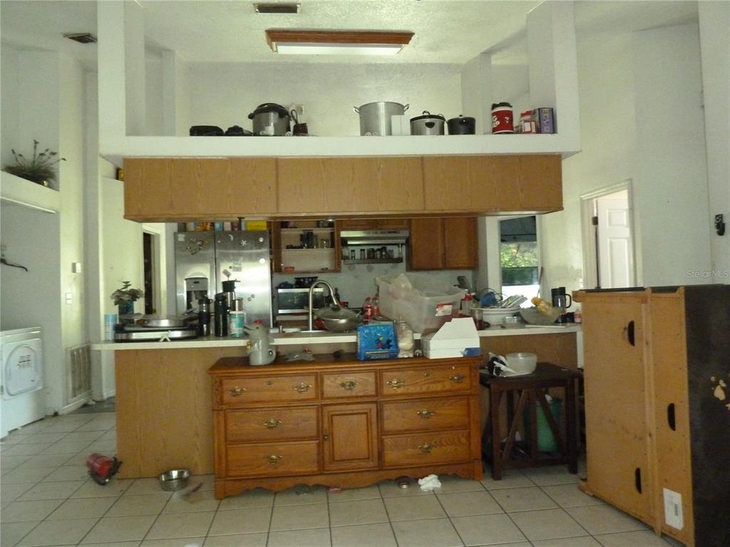 A kitchen features wooden cabinets, a breakfast bar with a dresser, and high ceilings — 5 S JUPITER AVENUE, CLEARWATER, FL