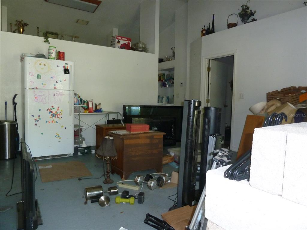 A cluttered room with a refrigerator, various furniture, and exercise equipment on a concrete floor — 5 S JUPITER AVENUE, CLEARWATER, FL