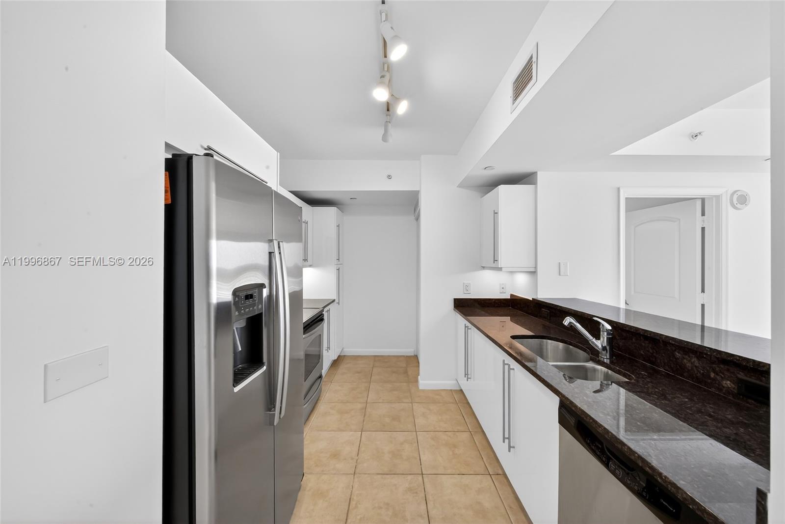 A kitchen features stainless steel appliances, white cabinetry, dark countertops, and light tile flooring — 7350 SW 89th St # 1703S, Miami FL 33156, MIAMI, FL
