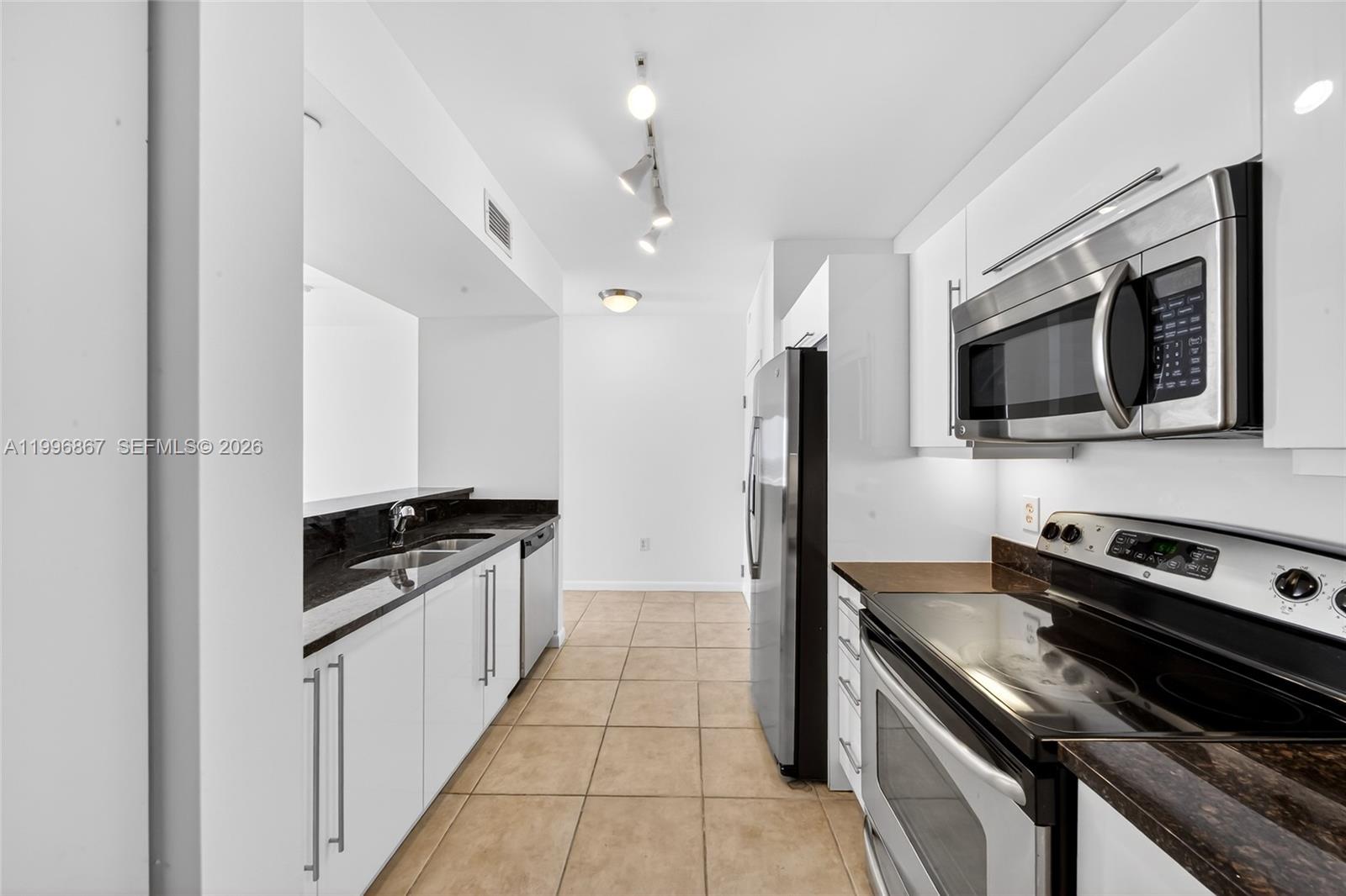 A galley kitchen features white cabinets, stainless steel appliances, and dark granite countertops — 7350 SW 89th St # 1703S, Miami FL 33156, MIAMI, FL