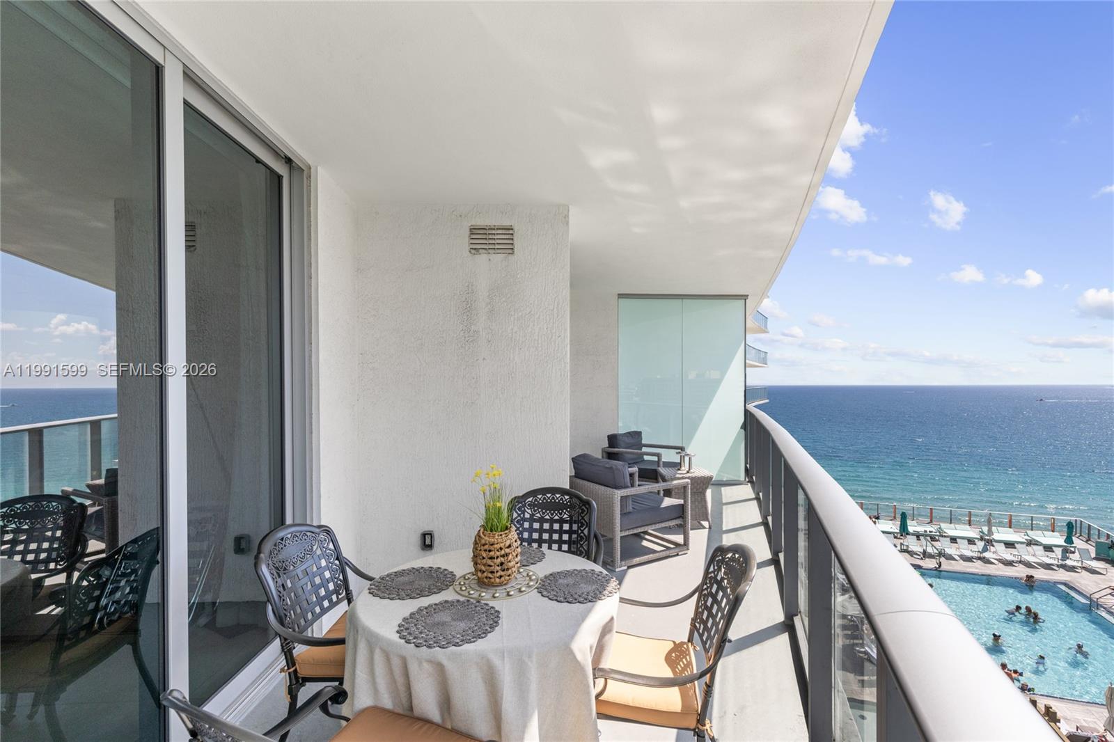 A balcony with outdoor furniture overlooks a swimming pool and the ocean — 4111 S Ocean Dr # 1107, Hollywood FL 33019, HOLLYWOOD, FL