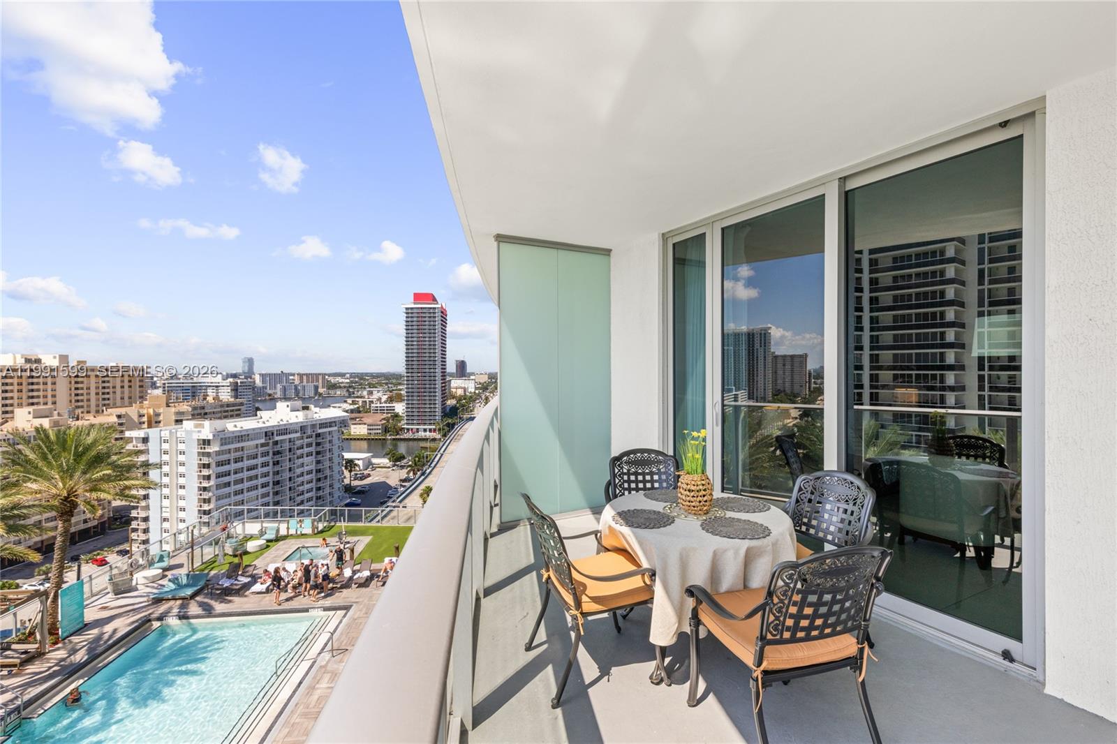 A balcony with a dining set overlooks a swimming pool and city skyline — 4111 S Ocean Dr # 1107, Hollywood FL 33019, HOLLYWOOD, FL