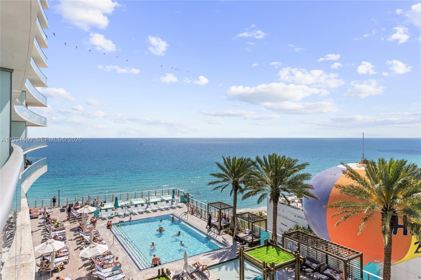 An elevated view of a swimming pool deck overlooking the ocean with palm trees — 4111 S Ocean Dr # 1107, Hollywood FL 33019, HOLLYWOOD, FL