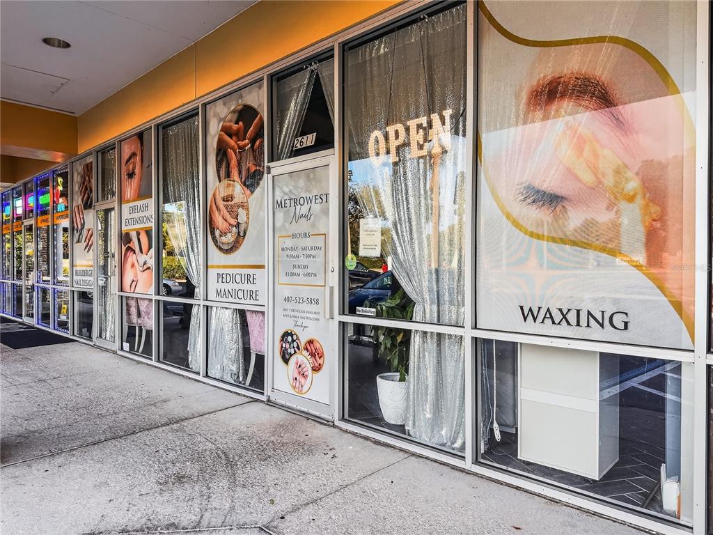 The exterior of a nail salon storefront features glass windows with service advertisements and hours — 2607 S HIAWASSEE ROAD, ORLANDO, FL