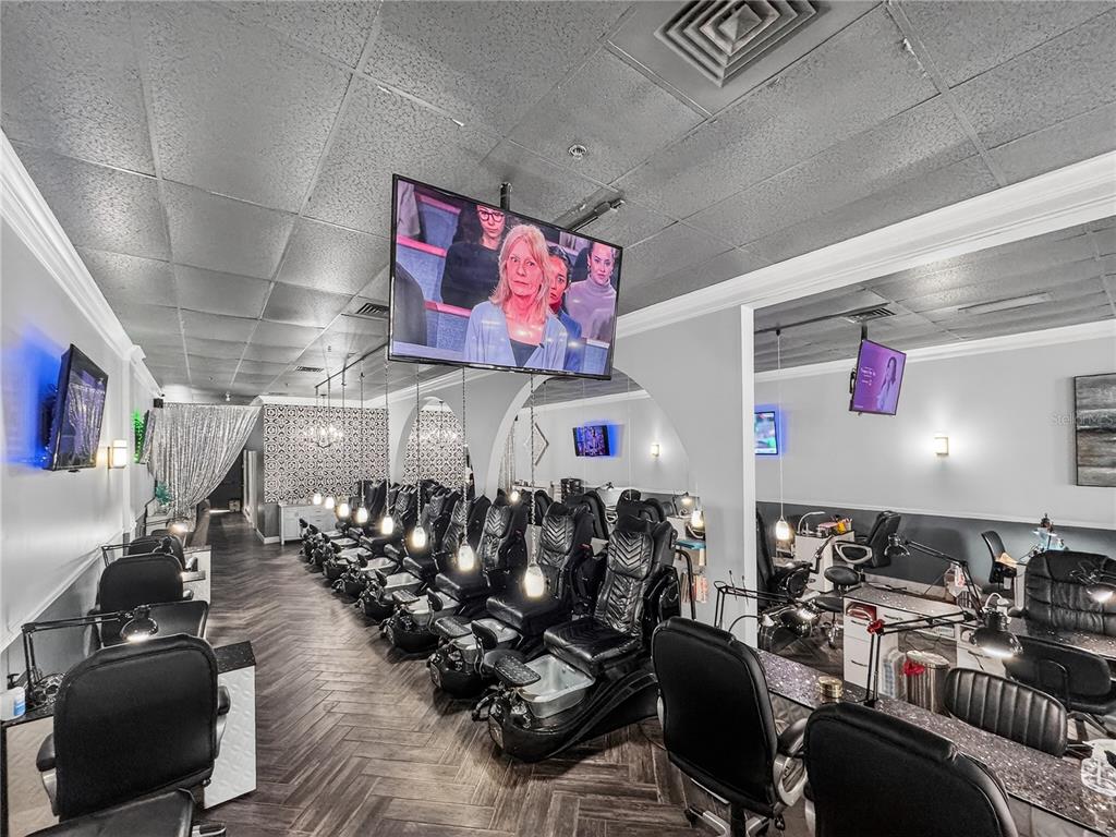 A nail salon interior features rows of black pedicure chairs, manicure stations, and ceiling-mounted televisions — 2607 S HIAWASSEE ROAD, ORLANDO, FL