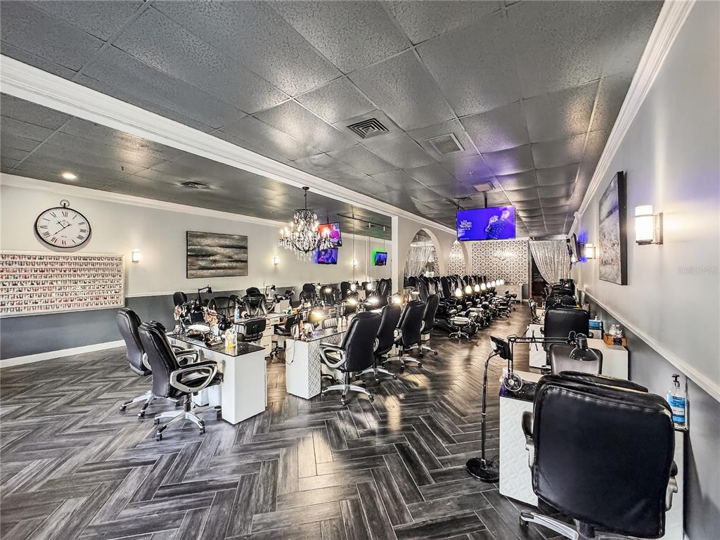 A nail salon features rows of manicure stations, pedicure chairs, and dark herringbone wood flooring — 2607 S HIAWASSEE ROAD, ORLANDO, FL